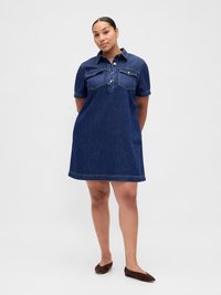Robe en denim à manches courtes, avec un col boutonné, deux poches poitrine et une coupe ample. Couleur bleu foncé avec une texture lisse.