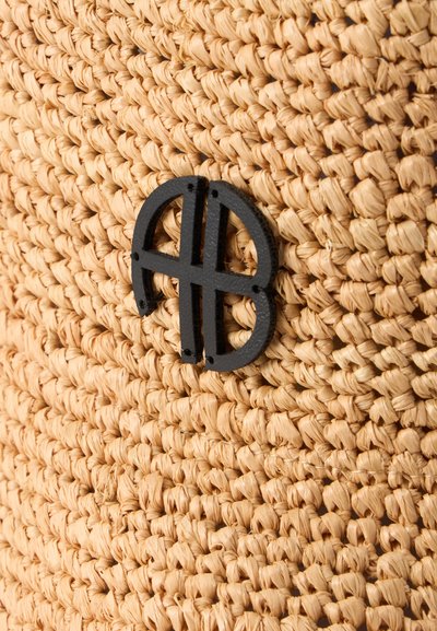 Gros plan sur un matériau en paille tressée avec un petit emblème décoratif noir, présentant des lignes courbes et droites qui se croisent, attaché dessus.