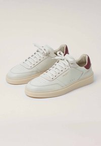 Sneaker bianche in pelle con dettagli beige chiaro, punta rotonda, tomaia perforata e accentuazione del tallone bordeaux. Lacci piatti e suola in gomma teksturizzata.