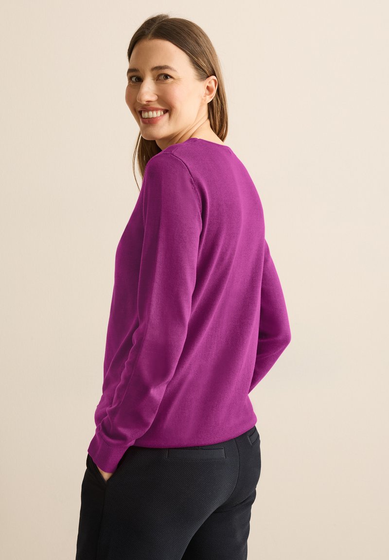 Pull à manches longues violet avec un col rond, fabriqué en matériau doux, associé à un pantalon noir texturé. Design simple sans motifs visibles.