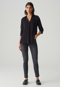 Blusa nera con colletto, caratterizzata da un design scollato a V e maniche lunghe. Abbinata a jeans slim-fit grigio scuro e mocassini neri.