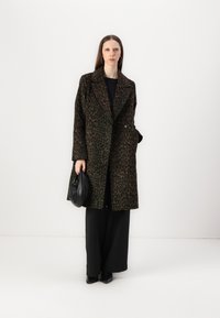 Manteau en laine imprimé léopard avec un design croisé, des revers larges et deux poches latérales, associé à un pantalon large noir et un sac.