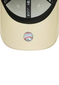 Gorra de béisbol beige con visera negra, que presenta un gráfico circular de una pelota de béisbol en la parte frontal. Tela texturizada y diseño estructurado.