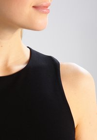 Top negro sin mangas con escote redondo, fabricado con un tejido elástico. La textura suave acentúa la clavícula y el hombro.