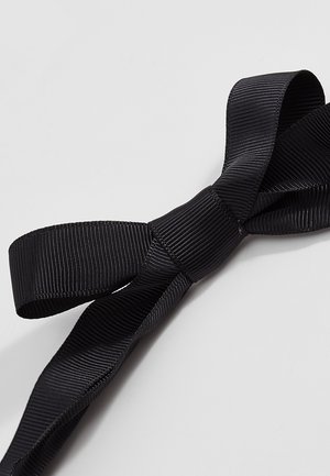 Schwarzes Grosgrain-Band, zu einer ordentlichen Schleife gebunden, mit sichtbarer gerippter Textur auf einer schlichten hellgrauen Oberfläche.