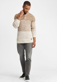 Pulover tricotat în bej și brown ombre cu guler henley, două butoane și manșete cu textură, asociat cu blugi gri și adidași negri.