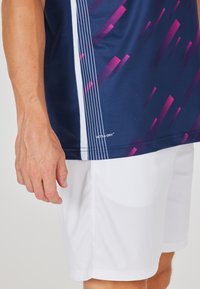 Marinblå träningströja med geometriskt rosa mönster, vita sidostråk och "ULTRA-DRY"-märke; kombinerad med vita shorts.