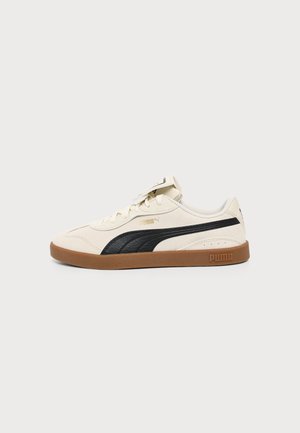 Baskets Puma crème avec une bande noire sur le côté et une semelle en gomme, vues de côté sur fond clair.