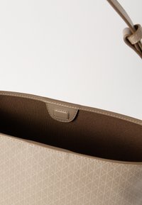 Μπεζ τσάντα tote με εξωτερικό μοτίβο, λεία υφή και σταθερό σχήμα. Το εσωτερικό είναι επενδυμένο με πιο σκούρο καφέ ύφασμα με ραφές λεπτομέρειες.