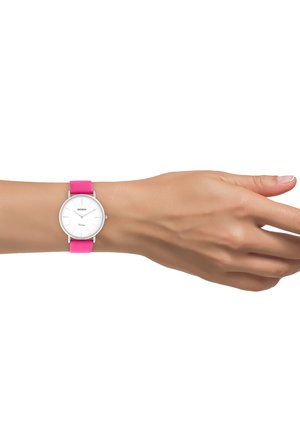 Poignet avec une montre analogique argentée, cadran blanc et bracelet en silicone rose, présenté sur un fond blanc.