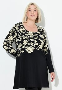 Zwarte tuniek jurk met lange mouwen, voorzien van een creme bloemenpatroon. Zacht materiaal, ronde halslijn en een ontspannen pasvorm.