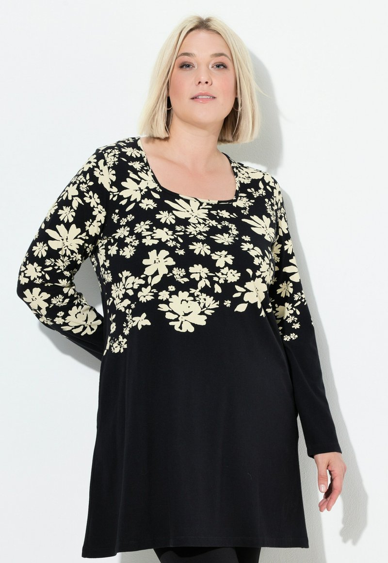 Zwarte tuniek jurk met lange mouwen, voorzien van een creme bloemenpatroon. Zacht materiaal, ronde halslijn en een ontspannen pasvorm.