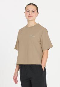 Ruskea lyhythihainen cropped t-paita, jossa on pyöreä kaula-aukko ja pieni valkoinen "LES ARCS" -painatus vasemmassa rinnassa.