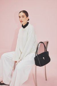 Črna usnjena torbica s strukturirano obliko in srebrnimi dodatki, v kombinaciji z oversized kremastim pletenim puloverjem in belimi širokimi hlačami.