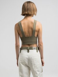 Olivgrünes geripptes Crop-Top mit breiten Trägern und einem tiefen Rückendesign. Kombiniert mit weißen Cargo-Hosen, ergänzt durch passende Gürteldetails.