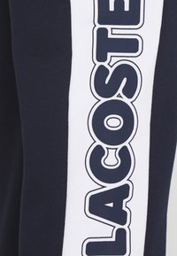 Marinblå sweatpants med en vit sidremsa och iögonfallande svart "LACOSTE"-tryck, mjuk textur och standard passform.