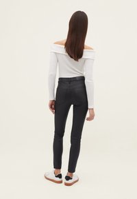 Svarta skinny jeans med bakfickor, som bärs med en vit off-shoulder topp. Har en slät textur och ankellång design. Vita sneakers med svarta detaljer.