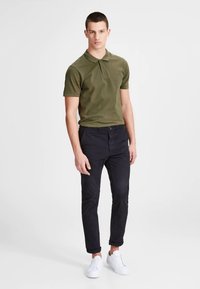 Grön pikétröja med krage, i kombination med mörka smala byxor och vita sneakers. Slät tyg med subtil textur.