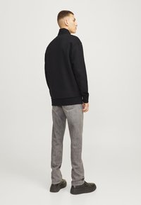 Black sweatshirt with high collar, loose fit. Paired with light gray denim jeans and black footwear, showcasing a simple, casual style.