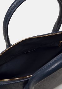 Granatowa skórzana torebka o teksturowanej powierzchni, z detalami w postaci złotego zamka błyskawicznego i przestronnym czarnym wnętrzem; wyposażona w dwa solidne uchwyty do noszenia.