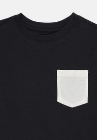 Black t-shirt with a crew neckline and a white fabric patch pocket on the left chest. Soft cotton material, minimalist design.