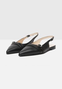 Sorte læder slingback sko med spidse tæer, der har en dekorativ rem og spænde samt en flad sål. Glat tekstur uden udsmykninger.