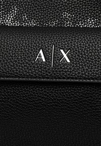 Borsa in pelle nera con texture, caratterizzata da un logo argentato "A/X" sul davanti. Il design è minimalista con una finitura elegante.