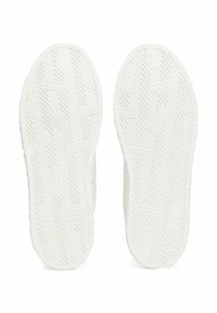 Suole di scarpe bianche in gomma con motivo a spina di pesce e designs testurizzati, caratterizzate da un bordo esterno liscio e una forma della punta arrotondata.