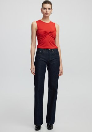 Top rosso senza maniche con dettaglio arricciato sulla parte anteriore, abbinato a jeans a gamba dritta blu scuro. Tessuto liscio e classica texture in denim.