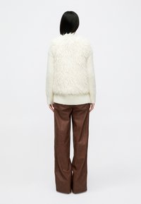 Sweater de malha grossa em creme com costas felpudas e texturizadas; combinado com calças longas em pele sintética castanha. Silhueta simples e relaxada.