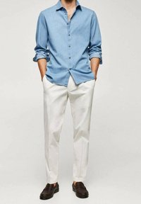 Chemise bleu clair à manches retroussées, associée à un pantalon blanc et des mocassins marron foncé. Style décontracté, coupe relax avec un design simple.