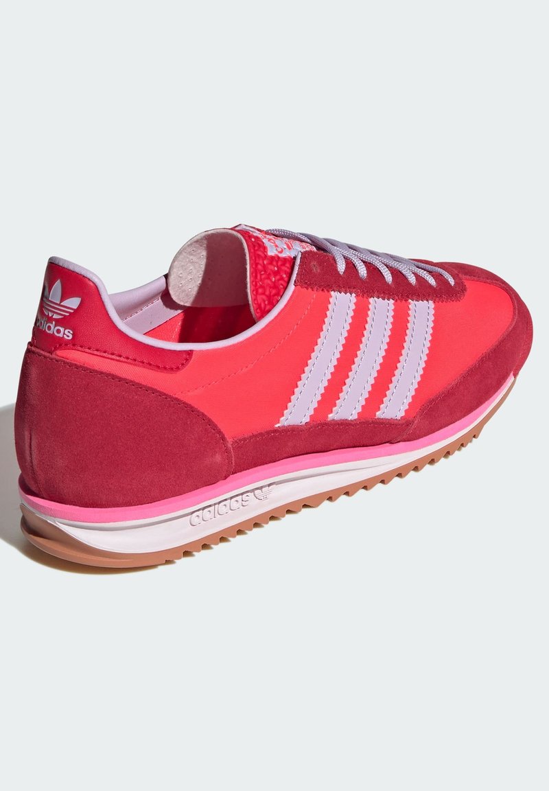 Zapatillas deportivas rojas y rosas que combinan materiales de ante y textil, tres franjas blancas y un talón texturizado con suela de goma.