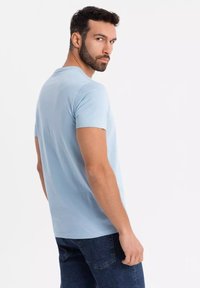 Světle modré tričko s krátkým rukávem vyrobené z bavlny. Má kulatý výstřih a volný střih, zobrazeno z boku s jemnými detaily šití.