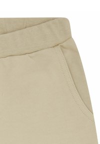 Beige katoenen broek met een zachte tailleband, voorzien van een zijzak en subtiele textuur, ontworpen voor comfort en gemakkelijk dragen.