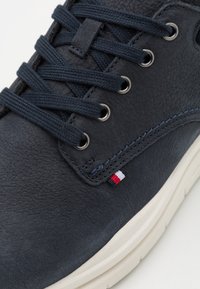 Granatowe skórzane sneakersy z okrągłymi sznurówkami, metalowymi oczkami, białą gumową podeszwą oraz małym akcentem logo w kolorach czerwonym, białym i niebieskim po boku.