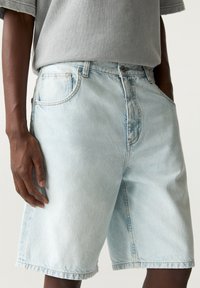 Vaaleansiniset farkkushortsit, joissa on väljä istuvuus, näkyvät taskupistot ja raakaremmi. Materiaali on hieman haalistuneen näköinen.