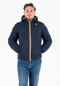 Giacca imbottita blu navy con zip, dettagli a strisce gialle e bianche e cappuccio. La giacca ha una texture liscia e presenta rifiniture a coste.