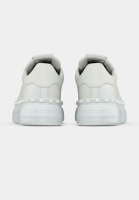 Λευκά αθλητικά παπούτσια με λείο δερμάτινο επάνω μέρος, επενδεδυμένο γιακά και υφή σόλας με διακοσμητικά τρουκ κατά μήκος της φτέρνας.