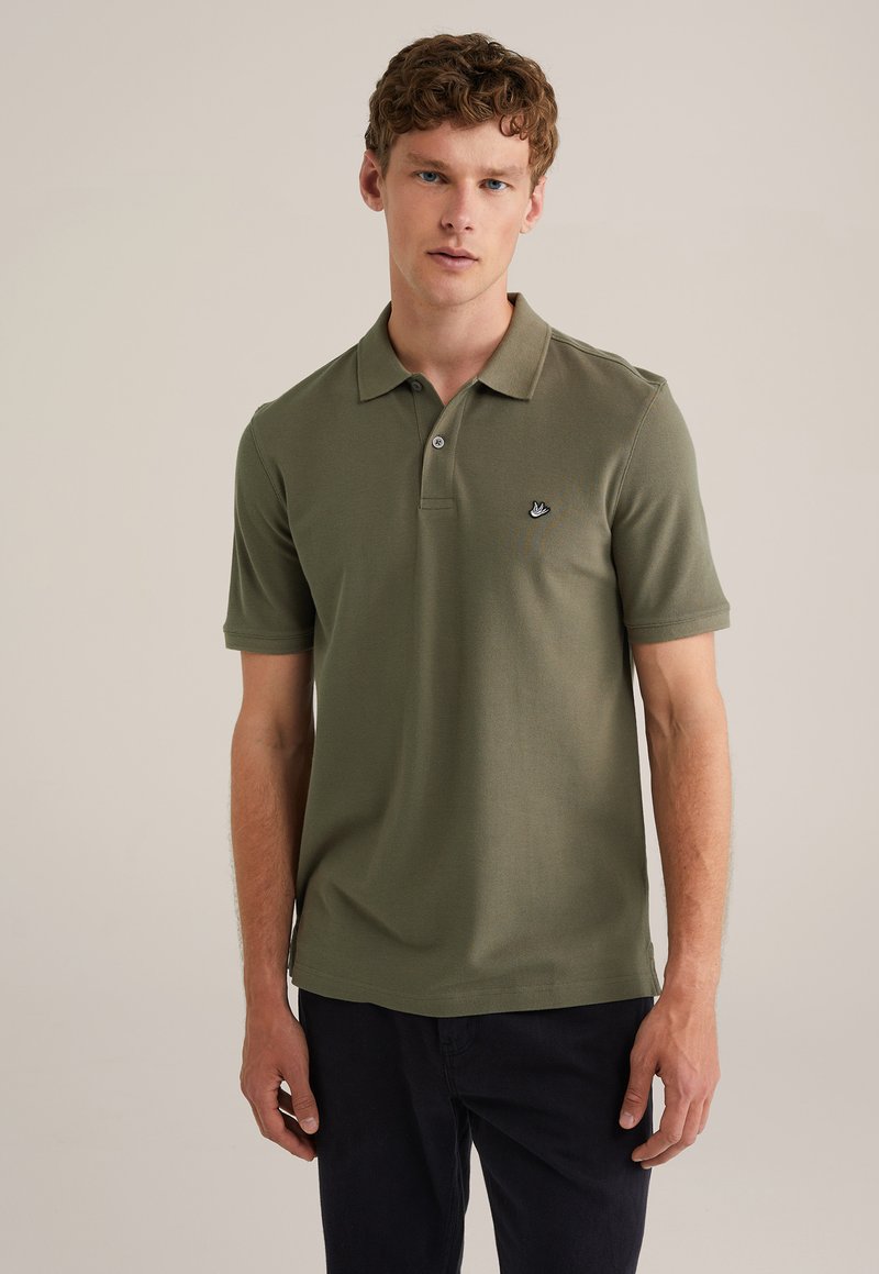 Polo in cotone verde oliva, maniche corte, colletto a due bottoni, con un piccolo logo nero sul lato sinistro del petto. Tessuto morbido.