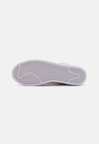 Weiße Sneaker-Sohle mit Fischgrätenmuster, ausgestattet mit einer helllila Gummibasis und einem glatten äußeren Rand. Rote Markenverzierung sichtbar.
