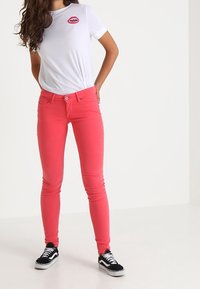 Slim-fit, jasně růžové džíny s předními kapsami, zapínáním na knoflík a poutky na opasek, spárované s bílým tričkem s barevným grafickým potiskem.