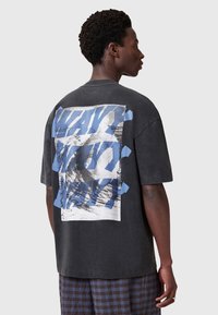 Sort oversized t-shirt med et stort grafisk print på ryggen i blå og hvid. Korte ærmer og afslappet pasform, med en vintage struktur.