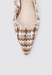Zapato de punta tejida en tonos de marrón, beige y blanco. Presenta una superficie texturizada con intrincados patrones trenzados.