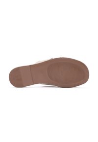Semelle en caoutchouc marron avec un grip à motifs, présentant un design plat. La partie supérieure est blanche, conçue pour un look décontracté.