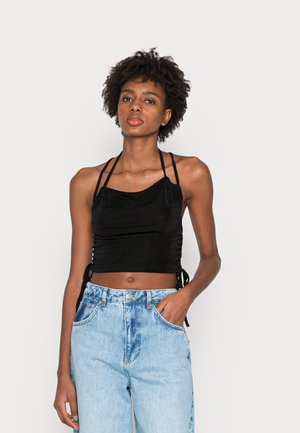 Top cropped preto com um design drapeado, laços laterais ajustáveis, usado com jeans de cintura alta azul claro, apresentando um ajuste descontraído e uma textura desbotada.