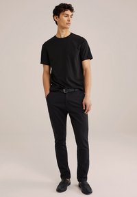 Fekete pamut póló és slim-fit fekete nadrág fekete loafers-el viselve. Egyszerű dizájn kerek nyakkivágással és sima textúrával.