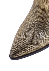 Zapato de tacón alto de punta afilada en dorado y negro. Cuenta con una superficie metálica texturizada con un patrón inspirado en reptiles y una suela negra.