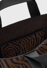 Hnědá taška přes rameno s texturovaným, zebrovým vzorem uvnitř a tmavou textilní podšívkou; má černé popruhy a měkké, filcovité materiály.