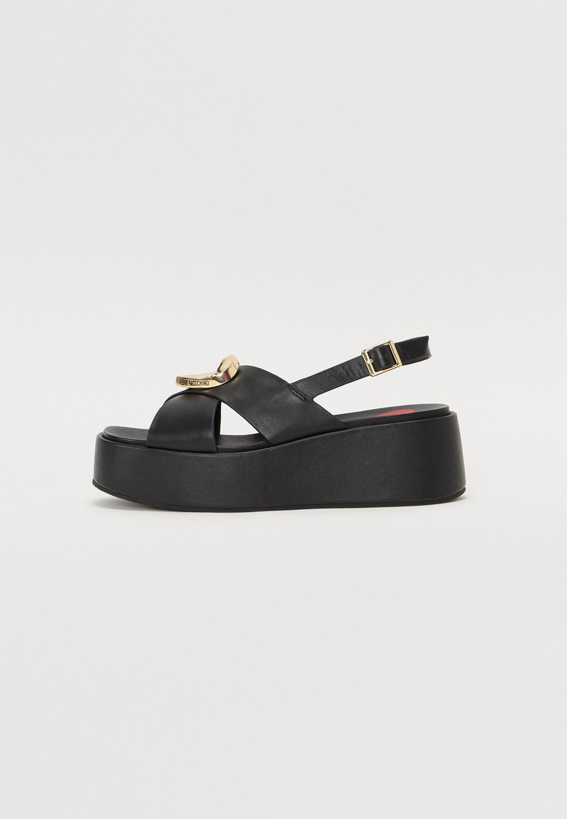 Black leather platform sandals with a cross-strap design and gold-tone hardware detail. Features an adjustable ankle strap and textured sole.