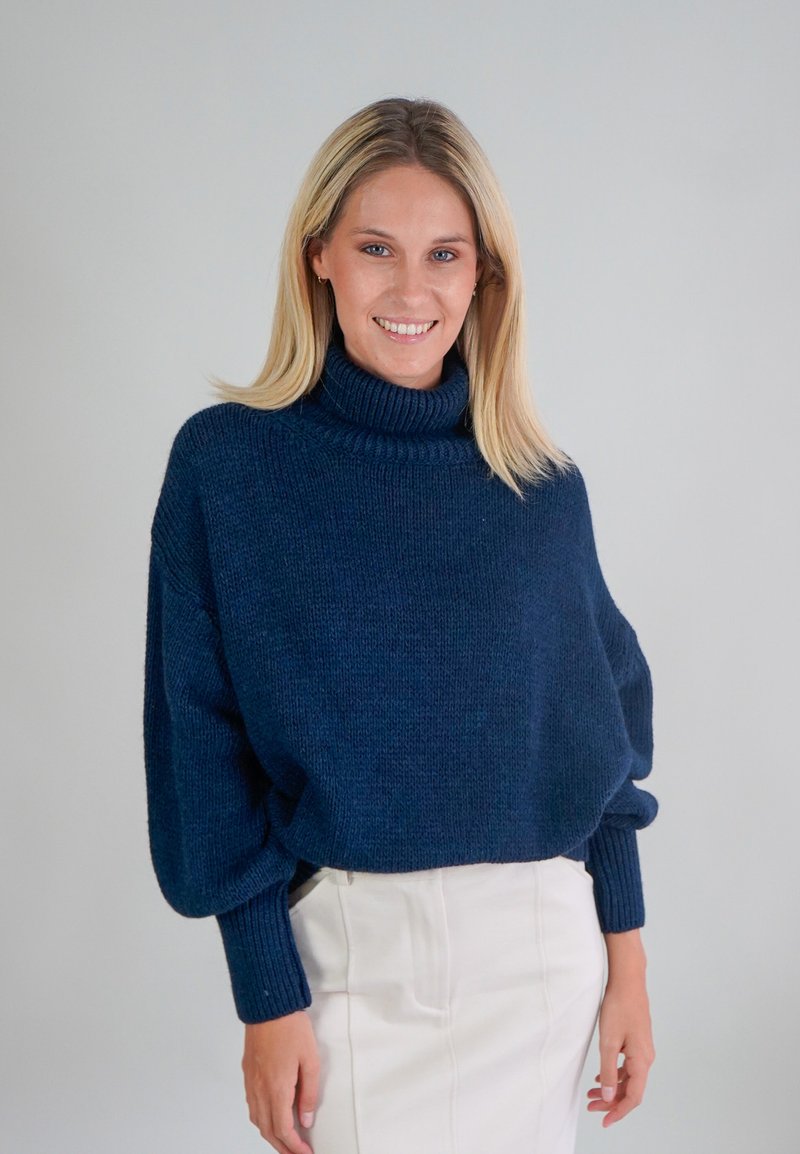 Navyblauwe oversized gebreide trui met een hoge col, verlaagde schouders en geribde manchetten. Zachte textuur met een ontspannen pasvorm.